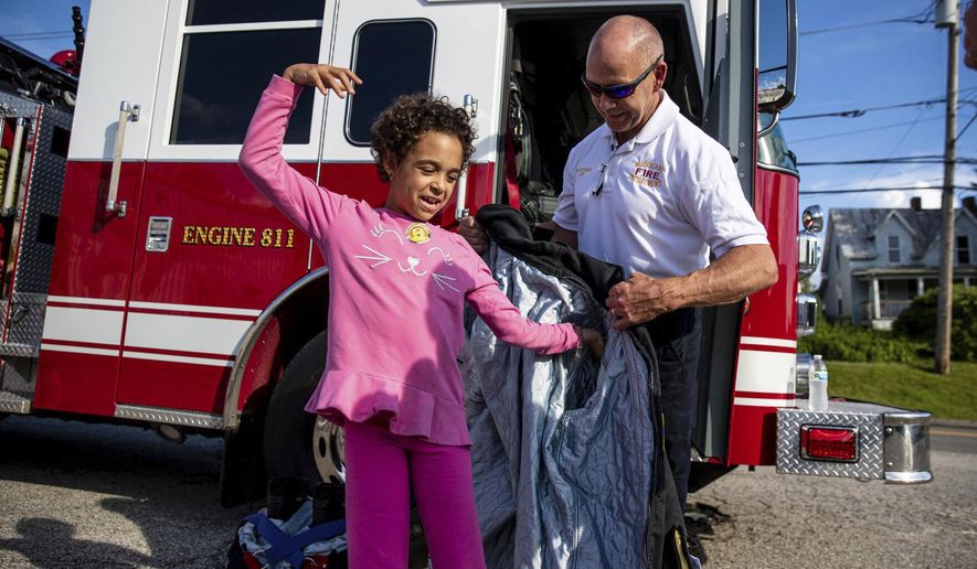 Hurricane Fire Chief Mike Hoffman helps 9-year-old Sophia Cossen try on a fireman’s jacket during the Hurricane Fire Department’s First Responders Meet and Greet sensory-friendly autism event on June 9, 2022, at the Hurricane Fire Department in Hurricane, W.Va. (Sholten Singer/The Herald-Dispatch via AP)
