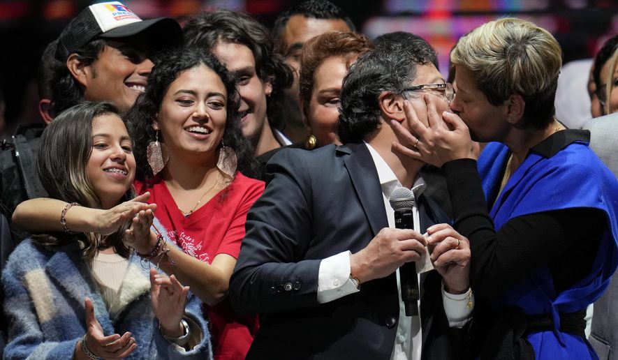 Veronica Alcocer kisses her husband, President-elect Gustavo Petro, under the look of their daughters Antonella, left, and Sofia as they celebrate before supporters after he won a runoff presidential election in Bogota, Colombia, Sunday, June 19, 2022. (AP Photo/Fernando Vergara)