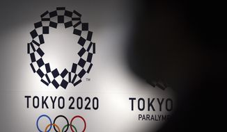 A person walks near Tokyo 2020 logo in Haneda Airport on June 14, 2021, in Tokyo. Tokyo Olympic officials, meeting Tuesday, June 21, 2022, before the body is dissolved at the end of the month, were to detail the final numbers that were driven up by the pandemic, but were in record range even before that. (AP Photo/Eugene Hoshiko, File)