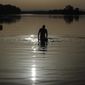 FILE - A man walks in the water as the sun rises above the Miribel lake, outside Lyon, central France, Saturday, June 18, 2022. A heat wave that&#39;s already lasted more than a week keeps on baking the US, Asia, Europe and even the Arctic. (AP Photo/Laurent Cipriani, File)