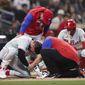 Philadelphia Phillies&#x27; Bryce Harper, left, receives attention after being hit by a pitch while interim manager Rob Thomson, background left, and Nick Castellanos, background right, look on during the fourth inning of the team&#x27;s baseball game against the San Diego Padres, Saturday, June 25, 2022, in San Diego. (AP Photo/Derrick Tuskan)