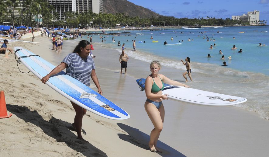 Two people with surf boards walk on Waikiki Beach, Thursday, June, 23, 2022 in Honolulu. In a major expansion of gun rights after a series of mass shootings, the Supreme Court said Thursday that Americans have a right to carry firearms in public for self-defense.