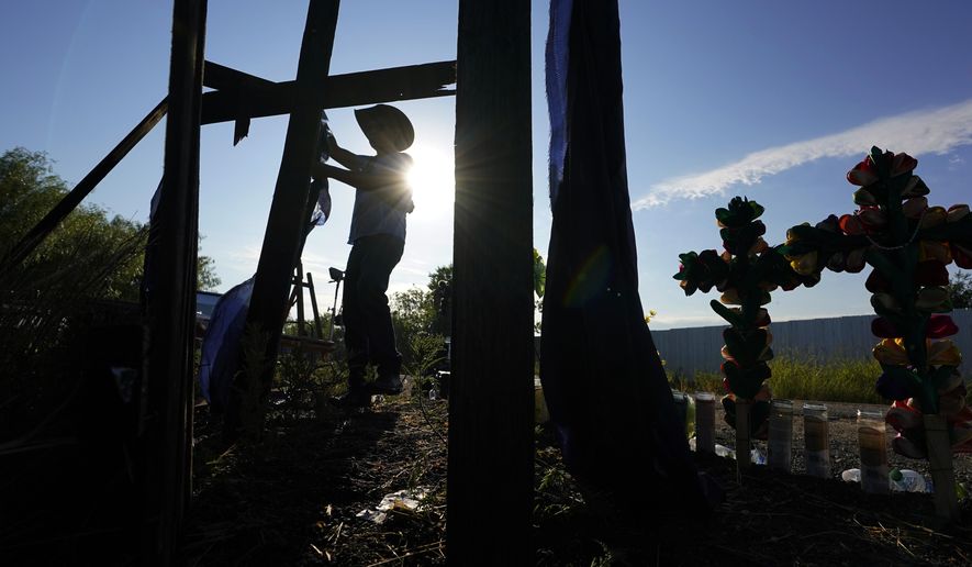 Roberto Marquez, of Dallas, adds a cross to a makeshift memorial at the site where officials found dozens of people dead in an abandoned semitrailer containing suspected migrants, Wednesday, June 29, 2022, in San Antonio. (AP Photo/Eric Gay)
