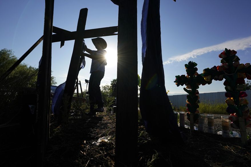 Roberto Marquez, of Dallas, adds a cross to a makeshift memorial at the site where officials found dozens of people dead in an abandoned semitrailer containing suspected migrants, Wednesday, June 29, 2022, in San Antonio. (AP Photo/Eric Gay)