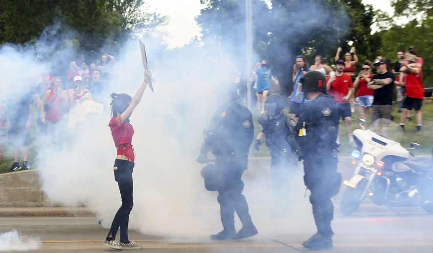 A protester holds a sign amid smoke from a police projectile during a protest against the Supreme Court decision overturning  Roe v. Wade on Wednesday, June 29, 2022, in Sioux Falls, S.D.  Police Chief Jon Thum said there were a “couple of arrests” during the demonstration. (Erin Woodiel /The Argus Leader via AP)