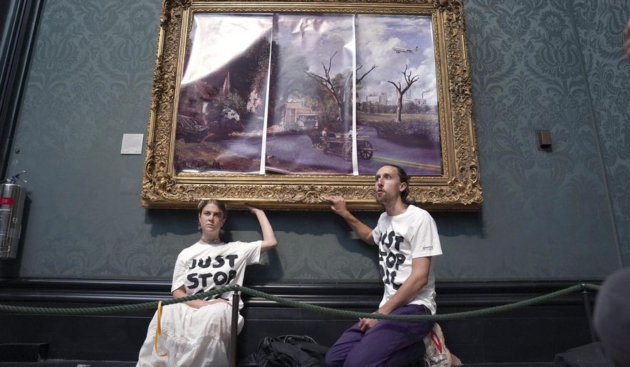 Protesters glue their hands to the frame of John Constable&#39;s The Hay Wain after first having covered the painting with their own picture, inside the National Gallery, London, Monday July 4, 2022. Police say two climate change protesters have been arrested after they glued themselves to the frame of a famous John Constable painting hanging in Britain’s National Gallery. The two, from the protest group “Just Stop Oil,” stepped over a rope barrier and covered “The Hay Wain” on Monday with large sheets of paper depicting “an apocalyptic vision of the future” of the landscape. (Kirsty O&#39;Connor/PA via AP)