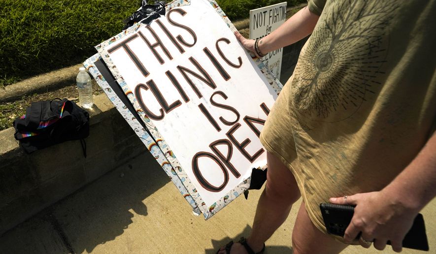 An abortion rights supporter carries away, the sign advising potential patients that the Jackson Women&#39;s Health Organization clinic was open in Jackson, Miss., Wednesday, July 6, 2022 (AP Photo/Rogelio V. Solis)