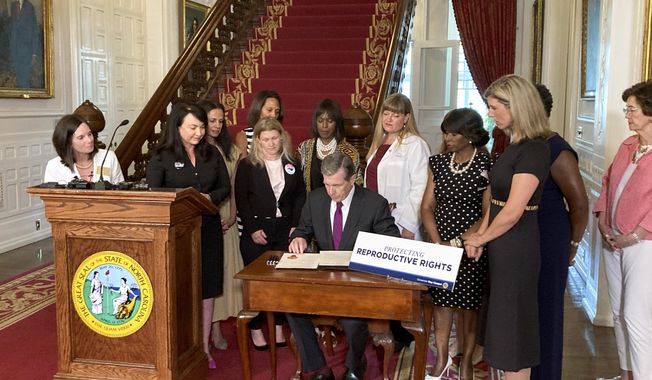 North Carolina Democratic Gov. Roy Cooper signs an executive order designed to protect abortion rights in the state at the Executive Mansion in Raleigh, N.C., on Wednesday, July 6, 2022. The order in part prevents the extradition of a woman who receives an abortion in North Carolina but who may live in another state where the procedure is barred. (AP Photo/Gary D. Robertson).