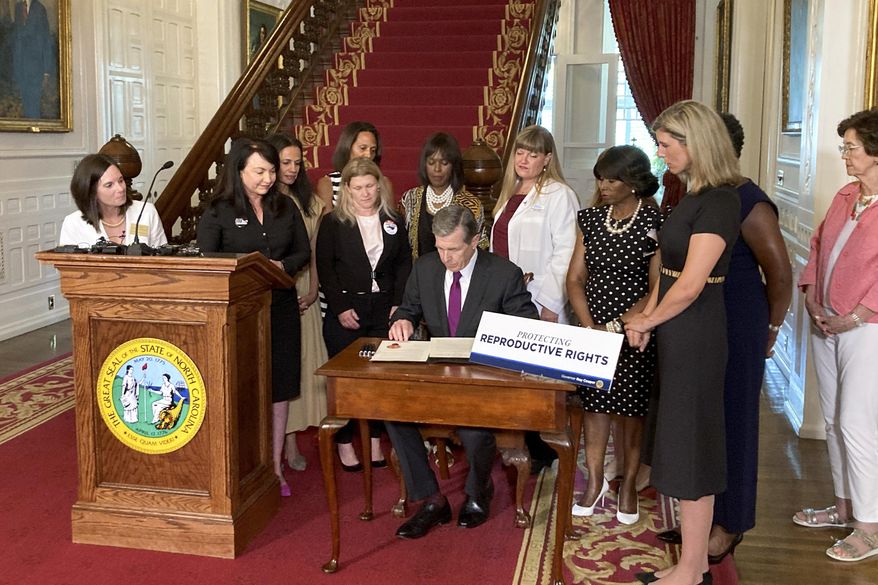 North Carolina Democratic Gov. Roy Cooper signs an executive order designed to protect abortion rights in the state at the Executive Mansion in Raleigh, N.C., on Wednesday, July 6, 2022. The order in part prevents the extradition of a woman who receives an abortion in North Carolina but who may live in another state where the procedure is barred. (AP Photo/Gary D. Robertson).