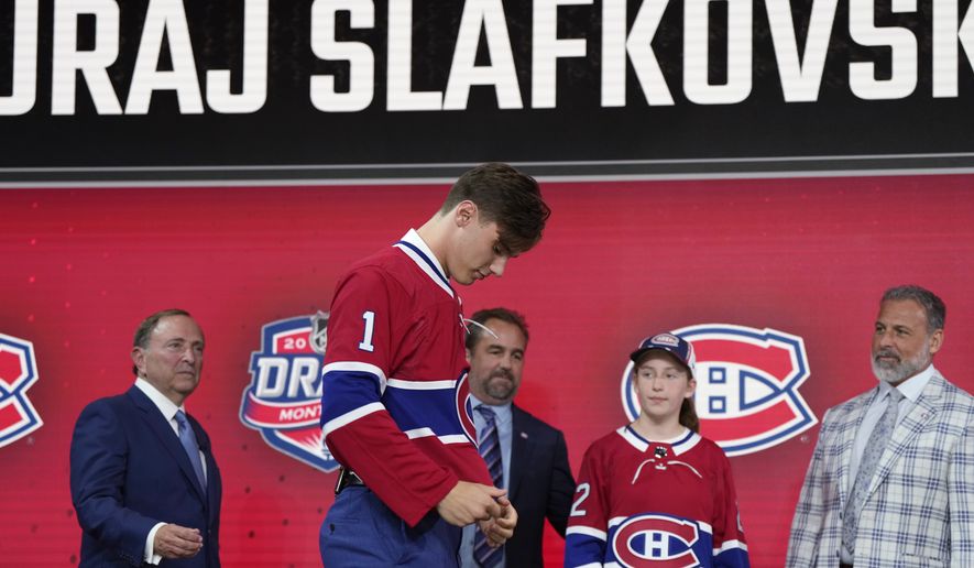 Juraj Slafkovsky puts on a Montreal Canadiens jersey after being selected as the top pick in the NHL hockey draft in Montreal on Thursday, July 7, 2022. Canadiens President and co-owner Geoff Molson is second from left in back. (Ryan Remiorz/The Canadian Press via AP)