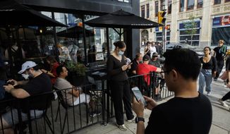 People use electronics outside a coffee shop in Toronto amid a nationwide Rogers outage, affecting many of the telecommunication company&#x27;s services, Friday, July 8, 2022. (Cole Burston/The Canadian Press via AP)