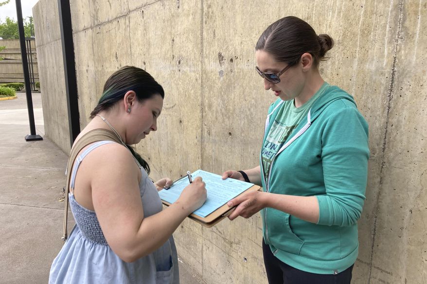 FILE - Raevahnna Richardson signs an initiative petition supporting a gun-safety ballot measure on June 7, 2022, outside a library in Salem, Ore., as signature gatherer Rebecca Nobiletti holds the clipboard. The Rev. Mark Knutson, a chief petitioner of the initiative, said the effort has gathered enough signatures of registered voters to put the measure before voters in the November election. After the signatures are delivered to the secretary of state's office, they will be verified by election officials. (AP Photo/Andrew Selsky, File)