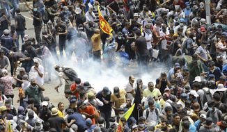 Protesters react as a tear gas shell fired by police lands next to them in Colombo, Sri Lanka, Saturday, July 9, 2022. Sri Lankan protesters demanding that President Gotabaya Rajapaksa resign forced their way into his official residence on Saturday, a local television report said, as thousands of people took to the streets in the capital decrying the island nation&#39;s worst economic crisis in recent memory. (AP Photo/Amitha Thennakoon)