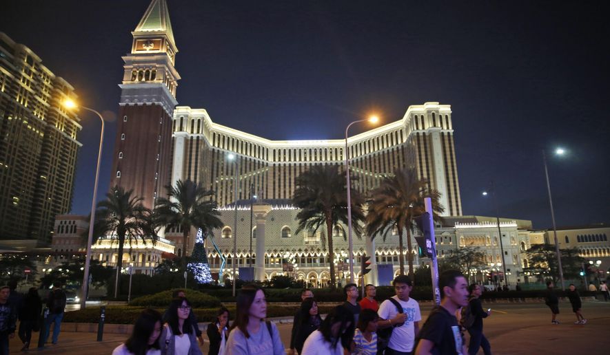 People walk in front of the Venetian Macao casino resorts in Macao, Nov. 23, 2014. The Asian gambling center of Macao will close all its casinos for a week starting Monday, July 11, and largely restrict people to their homes as it tries to stop a COVID-19 outbreak that has infected more than 1,400 people in the past three weeks. (AP Photo/Kin Cheung, File)