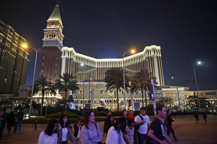 People walk in front of the Venetian Macao casino resorts in Macao, Nov. 23, 2014. The Asian gambling center of Macao will close all its casinos for a week starting Monday, July 11, and largely restrict people to their homes as it tries to stop a COVID-19 outbreak that has infected more than 1,400 people in the past three weeks. (AP Photo/Kin Cheung, File)