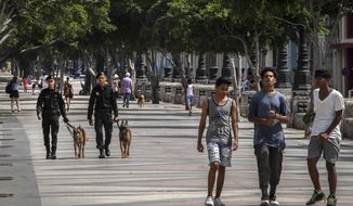 People walk at the Paseo del Prado while members of the police patrol in Havana, Cuba, Monday, July 11, 2022. A year after the largest protests in decades shook Cuba&#39;s single-party government, the economic and political factors that caused them largely remain. (AP Photo/Ramon Espinosa)