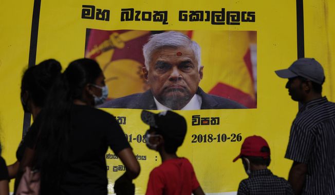 People watch propaganda materials displayed against prime minister Ranil Wickremesinghe outside president Gotabaya Rajapaksa&#x27;s office three days after it was stormed by anti government protesters in Colombo, Sri Lanka, Tuesday, July 12, 2022. (AP Photo/Eranga Jayawardena)