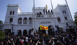 A protester, carrying national flag, stands with others on top of the building of Sri Lankan Prime Minister Ranil Wickremesinghe&#39;s office, demanding he resign after president Gotabaya Rajapaksa fled the country amid economic crisis in Colombo, Sri Lanka, Wednesday, July 13, 2022. Rajapaksa fled on a military jet on Wednesday after angry protesters seized his home and office, and appointed Prime Minister Ranil Wickremesinghe as acting president while he is overseas. Wickremesinghe quickly declared a nationwide state of emergency to counter swelling protests over the country&#39;s economic and political collapse. (AP Photo/Eranga Jayawardena)
