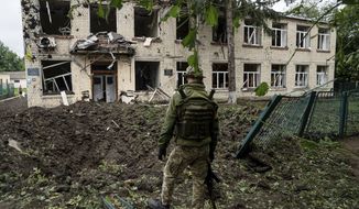 A Ukrainian serviceman looks at a crater and damaged school after Russian shelling in a residential area in Chuhuiv, Kharkiv region, Ukraine, Saturday, July 16, 2022. (AP Photo/Evgeniy Maloletka)