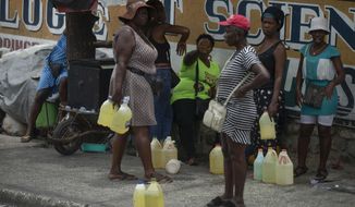 Women show their discomfort as they are being photographed selling contraband gasoline in plastic gallons jugs on a street in Port-au-Prince, Haiti, Thursday, July 14, 2022. (AP Photo/Odelyn Joseph)