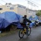 A person cycles past tents used by people experiencing homelessness set up along a pathway in Portland, Ore., on Sept. 19, 2017. (AP Photo/Ted S. Warren, File)