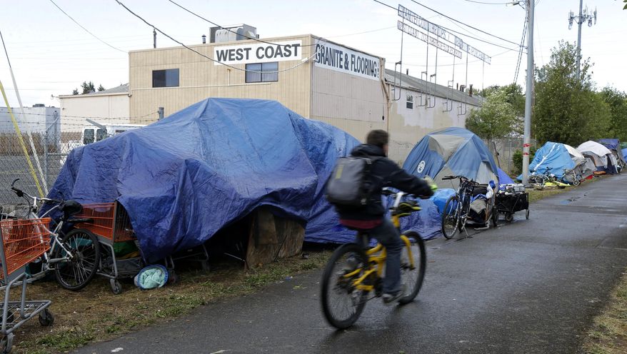 A person cycles past tents used by people experiencing homelessness set up along a pathway in Portland, Ore., on Sept. 19, 2017. (AP Photo/Ted S. Warren, File)