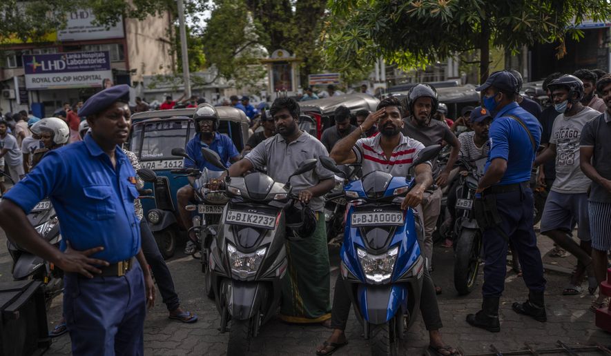 Police officers stand guard as people wait in queue to buy petrol at a fuel station, in Colombo, Sri Lanka, July 17, 2022. Bankruptcy has forced the island nation's government to a near standstill. Parliament is expected to elect a new leader Wednesday, paving the way for a fresh government, but it is unclear if that's enough to fix a shattered economy and placate a furious nation of 22 million that has grown disillusioned with politicians of all stripes. (AP Photo/Rafiq Maqbool)