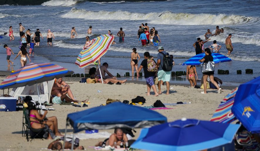 People enjoy the water at Rockaway Beach, Tuesday, July 19, 2022, in the Queens borough of New York. A number of factors, including warming ocean temperatures, are contributing to an expected proliferation of sharks along the New York coastline this summer. (AP Photo/Frank Franklin II)