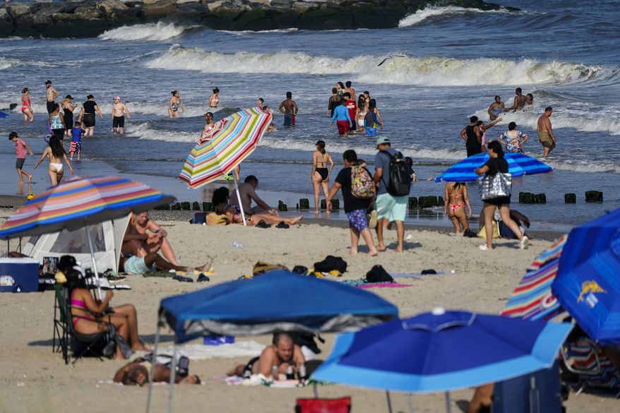 People enjoy the water at Rockaway Beach, Tuesday, July 19, 2022, in the Queens borough of New York. A number of factors, including warming ocean temperatures, are contributing to an expected proliferation of sharks along the New York coastline this summer. (AP Photo/Frank Franklin II)
