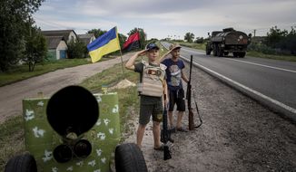 Maksym and Andrii 11, years old boys, salute to Ukrainian soldiers holding plastic guns as they play at the self-made checkpoint on the highway in Kharkiv region, Ukraine, Wednesday, July 20, 2022. (AP Photo/Evgeniy Maloletka)