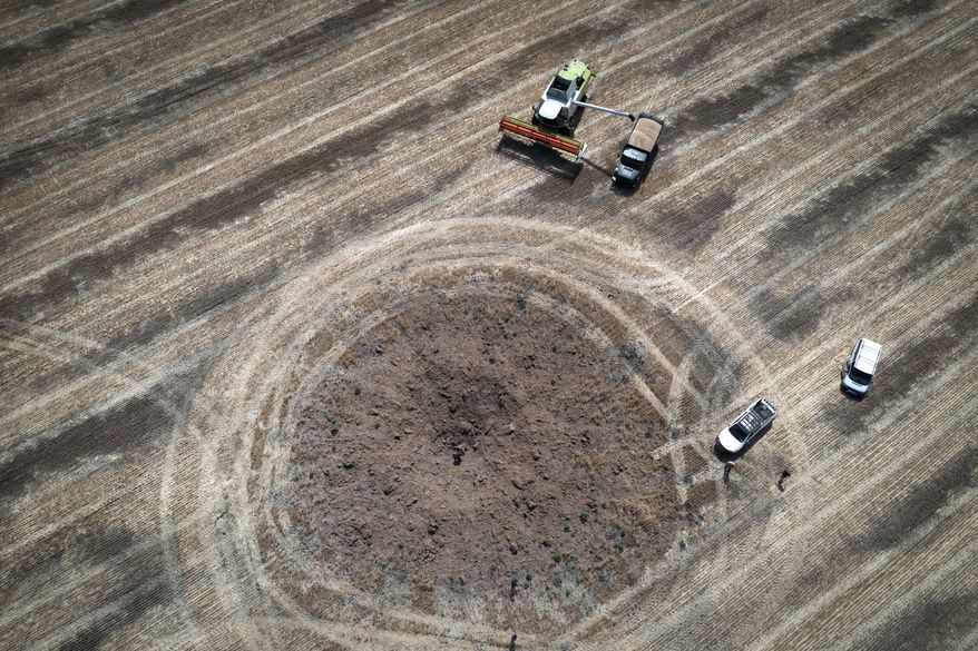 A farmer collects harvest on a field around a crater left by a Russian rocket 10 kilometers from the front line in the Dnipropetrovsk region, Ukraine, on July 4, 2022. Turkish officials say a deal on a U.N. plan to unblock the exports of Ukrainian grain amid the war and to allow Russia to export grain and fertilizers will be signed Friday, July 22, 2022, in Istanbul. (AP Photo/Efrem Lukatsky) **FILE**