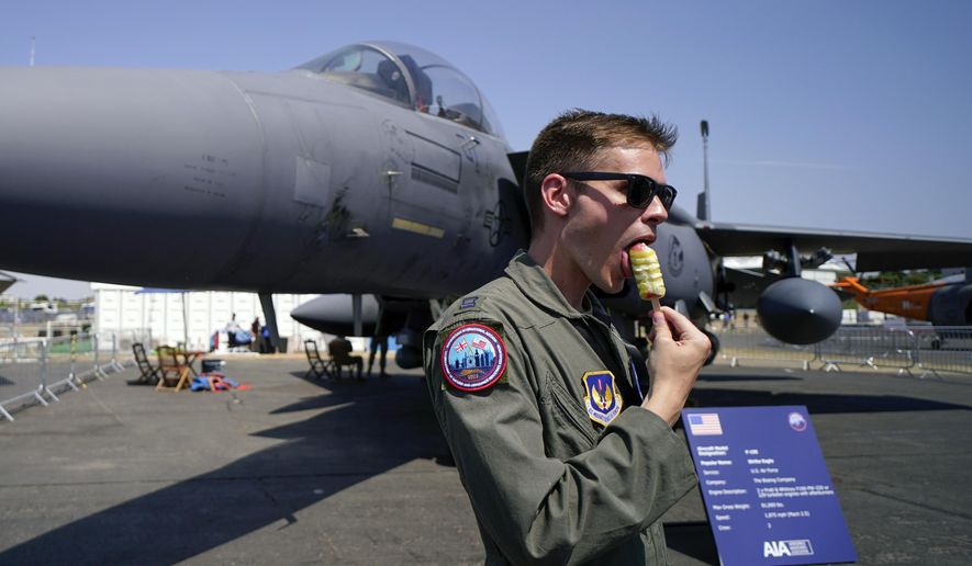 A member of the military personnel eats an ice cream as he stands past an F15E Strike Eagle fighter jet, on display at the Farnborough Air Show fair in Farnborough, England, Tuesday, July 19, 2022. The future for fighter pilots was on display at the Farnborough International Airshow near London, one of the world’s biggest aviation, defense and aerospace expos. New technologies take on a bigger role in the cockpit, redefining what it means to be a &#x27;&#x27;Top Gun.&#x27;&#x27; (AP Photo/Alberto Pezzali, File)