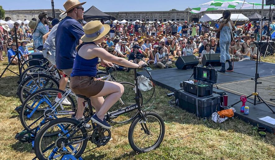 Madi Diaz, right, performs at the Newport Folk Festival&#39;s bike stage, powered in part by festivalgoers on stationary bicycles, left, Friday, July 22, 2022, in Newport, R.I. (AP Photo/Pat Eaton-Robb)