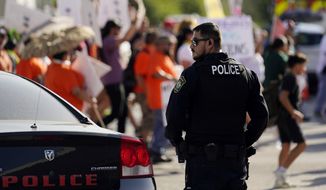 A Uvalde police officer watches as family and friends of those killed and injured in the school shootings at Robb Elementary take part in a protest march and rally, Sunday, July 10, 2022, in Uvalde, Texas. Families and residents are seeking answers and changes after the tragedy. (AP Photo/Eric Gay)