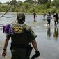 A Border Patrol agent watches as a group of migrants walk across the Rio Grande on their way to turn themselves in upon crossing the U.S.-Mexico border in Del Rio, Texas, on June 15, 2021. The Supreme Court has certified its month-old ruling allowing the Biden administration to end a cornerstone Trump-era border policy to make asylum-seekers wait in Mexico for hearings in U.S. immigration court. It was a pro forma act that has drawn attention amid near-total silence from the White House about when, how and even whether it will dismantle the policy. (AP Photo/Eric Gay) **FILE**