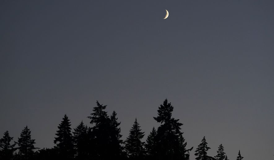 A crescent moon rises above trees, Tuesday, Aug. 2, 2022, in Issaquah, Wash., east of Seattle. (AP Photo/Ted S. Warren)