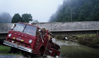 A fire truck is seen hangin over the edge of the water propped against a bridge on Wednesday, Aug. 3, 2022, in Hindman, Ky., after massive flooding carried the fire truck towards the water.  Temperatures are soaring in a region of eastern Kentucky where people are shoveling out the wreckage of massive flooding. (AP Photo/Brynn Anderson)