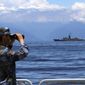In this photo provided by China’s Xinhua News Agency, a People&#39;s Liberation Army member looks through binoculars during military exercises as Taiwan’s frigate Lan Yang is seen at the rear, on Friday, Aug. 5, 2022. China is holding drills in waters around Taiwan in response to a recent visit by U.S. House Speaker Nancy Pelosi. (Lin Jian/Xinhua via AP)