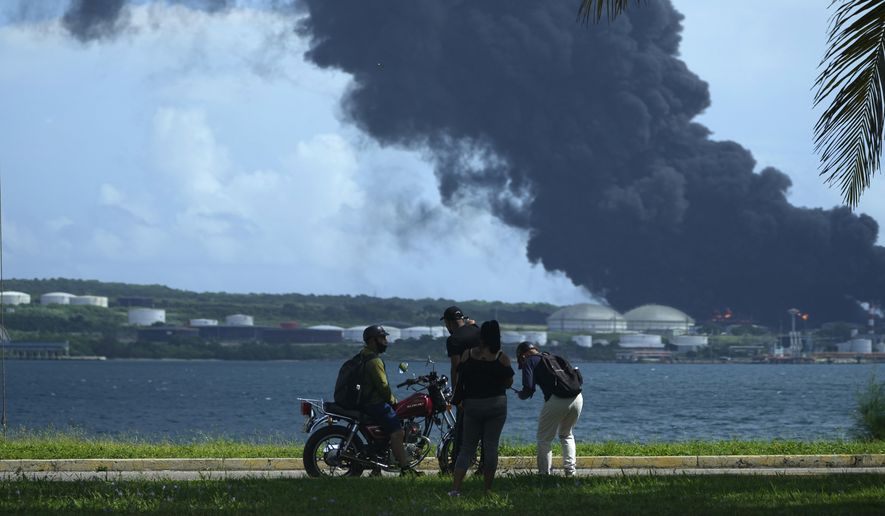 People watch a huge rising plume of smoke from the Matanzas Supertanker Base, as firefighters try to quell a blaze which began during a thunderstorm the night before, in Matazanas, Cuba, Saturday, Aug. 6, 2022. Cuban authorities say lightning struck a crude oil storage tank at the base, causing a fire that led to four explosions which injured more than 50 people. (AP Photo/Ramon Espinosa)