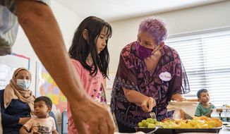 Nancy Kramer, a teacher from the Westminster Shores senior living facility, serves a plate of fruit to Hasina Sharifi, 8, of the Jawzjan province in Afghanistan on Wednesday, June 29, 2022 in St. Petersburg, Fla. Kramer, along with other residents of the senior living facility, will teach refugee children from Afghanistan how to read, write, and speak in English and other subjects such as arithmetic and science. (Angelica Edwards/Tampa Bay Times via AP)