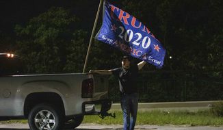 A man who declined to provide his name stands by a flag expressing support for former President Donald Trump near his Mar-a-Lago estate in Palm Beach, Fla., Monday, Aug. 8, 2022. The FBI has searched the estate as part of an investigation into whether he took classified records from the White House to his Florida residence. (Andres Leiva/The Palm Beach Post via AP)