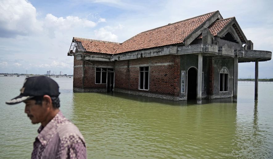 A man walks past a house abandoned after it was inundated by water due to the rising sea level in Sidogemah, Central Java, Indonesia, Nov. 8, 2021. Climate hazards such as flooding, heat waves and drought have worsened more than half of the hundreds of known infectious diseases in people, such as malaria, hantavirus, cholera and even anthrax, according to a new study released Monday, Aug. 8, 2022. (AP Photo/Dita Alangkara, File)