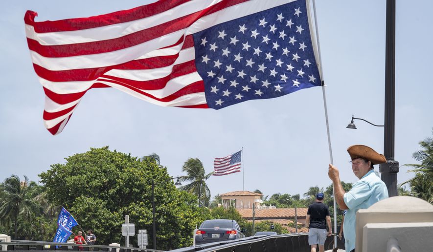 Ben Pollack holds his flag upside down as he stands near Mar-a-Lago, in background, in Palm Beach, Fla., on August 9, 2022. (Greg Lovett/The Palm Beach Post via AP)