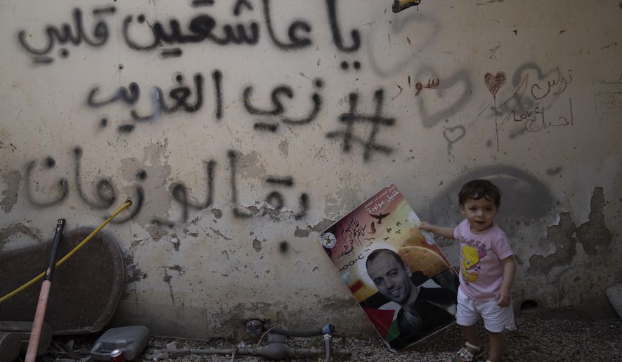 Maryam holds a poster showing her father Khalil Awawdeh, a Palestinian prisoner in Israel, at the family house in the West Bank village of Idna, Hebron, Tuesday, Aug. 9, 2022. Arabic graffiti reads: &amp;quot;to those who are in love, my heart is like a stranger, it is a long time.&amp;quot; Awawdeh who has refused food for 150 days and is wasting away in an Israeli jailhouse infirmary has suddenly been thrust at the center of efforts to firm up a Gaza cease-fire. (AP Photo/Nasser Nasser)