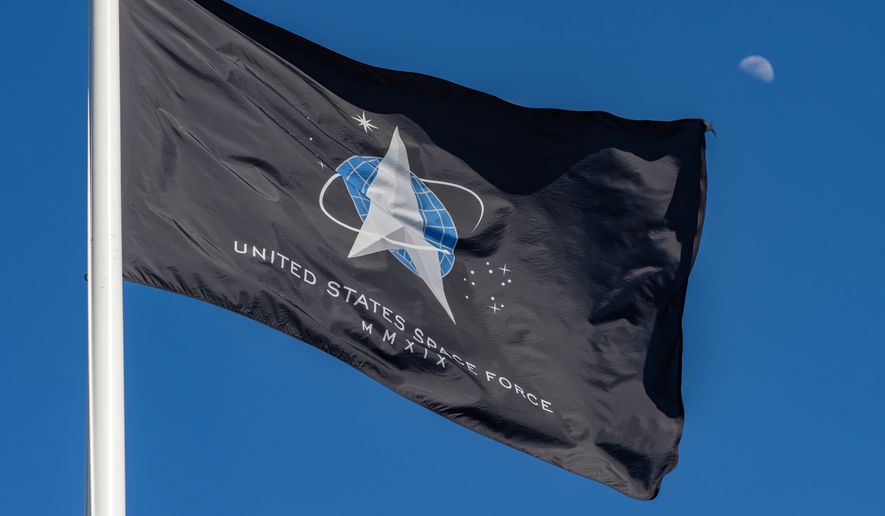 The flag of the United States Space Force flies high on a sunny afternoon as a half moon rises behind it. File photo credit: Ajax9 via Shutterstock.