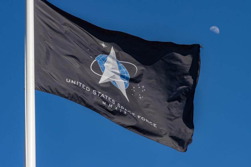 The flag of the United States Space Force flies high on a sunny afternoon as a half moon rises behind it. File photo credit: Ajax9 via Shutterstock.