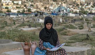 Sara, a 14-year-old, an Afghan girl, sits on a grave and reads a book as she waits for customers to sell water at a cemetery, in Kabul, Afghanistan, Saturday, July 30, 2022. For most teenage girls in Afghanistan, it’s been a year since they set foot in a classroom. With no sign the ruling Taliban will allow them back to school, some girls and parents are trying to find ways to keep education from stalling for a generation of young women. (AP Photo/Ebrahim Noroozi)