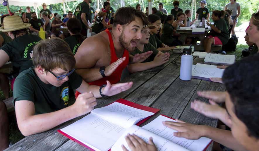 In this Aug. 4, 2022 photo, Mid-Atlantic Burn Camp counselor Logan Monk, of Goochland, Va., leads his table in singing camp songs after lunch at Camp Brethren Woods in Keezletown, Va. Monk, 24, has attended the camp for 15 years and is in his 7th year as a counselor. (Daniel Lin/Daily News-Record via AP)