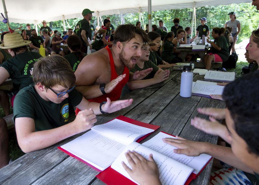 In this Aug. 4, 2022 photo, Mid-Atlantic Burn Camp counselor Logan Monk, of Goochland, Va., leads his table in singing camp songs after lunch at Camp Brethren Woods in Keezletown, Va. Monk, 24, has attended the camp for 15 years and is in his 7th year as a counselor. (Daniel Lin/Daily News-Record via AP)