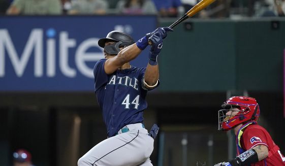 Seattle Mariners&#39; Julio Rodriguez (44) follows through on a two-run single next to Texas Rangers catcher Jonah Heim during the fourth inning of a baseball game in Arlington, Texas, Friday, Aug. 12, 2022. (AP Photo/Tony Gutierrez)